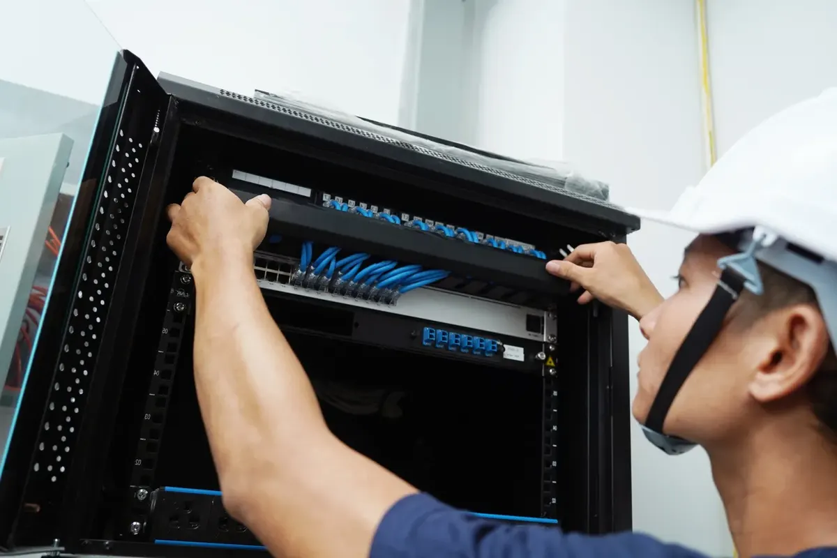 Engineer installing network cabling in a comms cabinet